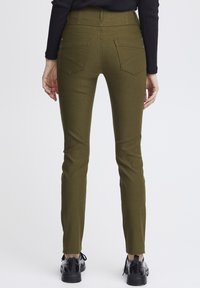 Olivově zelené skinny kalhoty s vysokým pasem, které mají dvě zadní kapsy a hladkou, elastickou strukturu, doplněné černými botami.