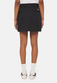 Černá sukně s úzkým pasem, dvěma zadními kapsami a páskem. Vyrobena z hladkého materiálu, navržena pro neformální vzhled. Minimální detaily, čisté linie.