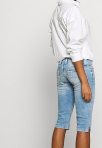 Bermudas de denim azul claro de corte ajustado, con una textura desgastada y dobladillo enrollado. Combinadas con una camisa blanca de corte holgado.