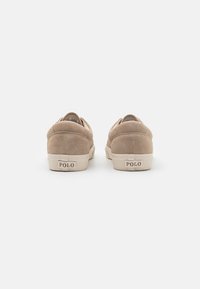 Beżowe zamszowe sneakersy o niskim profilu, zaokrąglonym tyle i gumowej podeszwie. Posiadają widoczne logo "POLO" na pięcie. Miękka tekstura.