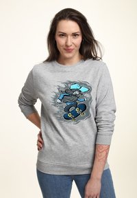 Felpa grigia con una grafica vivace di uno skater. Presenta polsini e orlo a coste, e una texture morbida. Abbinata a jeans blu.