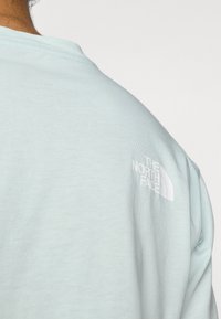 Γαλάζιο βαμβακερό μπλουζάκι με λευκό λογότυπο The North Face στο πάνω δεξί μέρος, με στρογγυλή λαιμόκοψη και κοντά μανίκια.