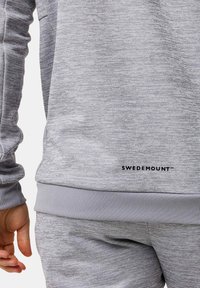 Grauer Sweatshirt mit strukturiertem Stoff, geripptem Saum und Bündchen. Mit einem schwarzen "SWEDEMOUNT"-Logo nahe dem Saum. Das Material wirkt weich und lässig.