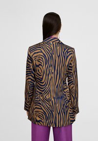 Brown and navy patterned blazer with pronounced zebra stripes, tailored fit, shoulder pads, and button accents on sleeves.