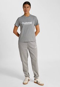 Grå t-shirt och grå mjukisbyxor set. T-shirten har en stor vit varumärkeslogga; byxorna har en mindre logga. Bomullsblandning, avslappnad passform.