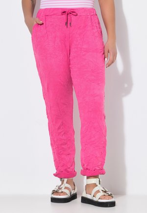 Osoba nosząca jasnoróżowe, teksturowane spodnie z podwiniętymi mankietami, białe sandały na platformie oraz różowo-biały pasiasty top z ręką w kieszeni.