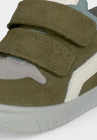 Κοντινή λήψη ελαιοπράσινου suede sneaker με δύο λουριά Velcro, λευκή πλαϊνή ρίγα και ανοιχτό γκρι λαστιχένια σόλα.