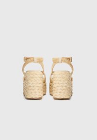 Sandalias de cuña hechas de fibras naturales trenzadas, con una correa beige con hebilla y un diseño de talón abierto.