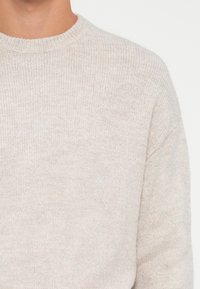 Lys grå strikket sweater med rund halsudskæring, ribbede ærmer og en blød tekstur med et subtilt mønster. Hyggeligt og afslappet design.