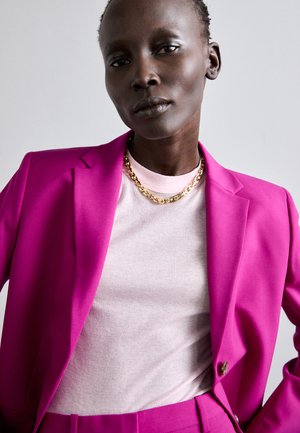 Fuchsia tailored blazer with matching trousers over a light pink ribbed top, featuring gold chain jewelry, contributing bold color contrast.