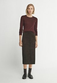 Burgundy långärmad topp i kombination med en mörkgrön mocka midi-kjol. Outfiten har figursydda ärmar och texturerade material. Svarta loafers kompletterar looken.
