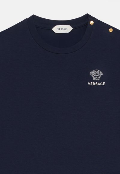 Μπλε σκούρο πουκάμισο Versace με στρογγυλή λαιμόκοψη, κέντημα με το λογότυπο της Μέδουσας και το όνομα της μάρκας στο στήθος, καθώς και δύο χρυσά κουμπιά στον ώμο.