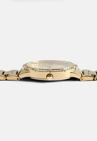 Relógio em tom dourado com mostrador redondo, embellishments de cristal em volta do bezel e uma bracelete de metal ligada. Apresenta uma coroa de lado.