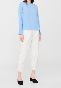 Lyseblå langærmet skjorte med en afslappet pasform, parret med hvide stribede ankelbukser og sorte blokhælede sko.