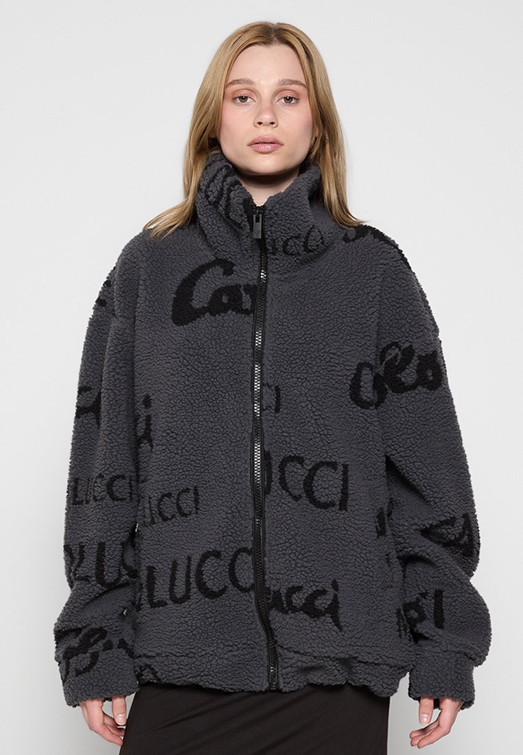 Grijze fleece jas met een hoge kraag, voorzien van een ritssluiting en een herhaald zwart logo-tekstpatroon. Losse pasvorm met brede mouwen.