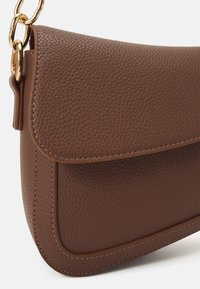 Borsa a mano in pelle marrone con una texture a chicchi, silhouette curva e pattina pieghevole, dotata di accenti in hardware dorato e dettagli di cucitura.