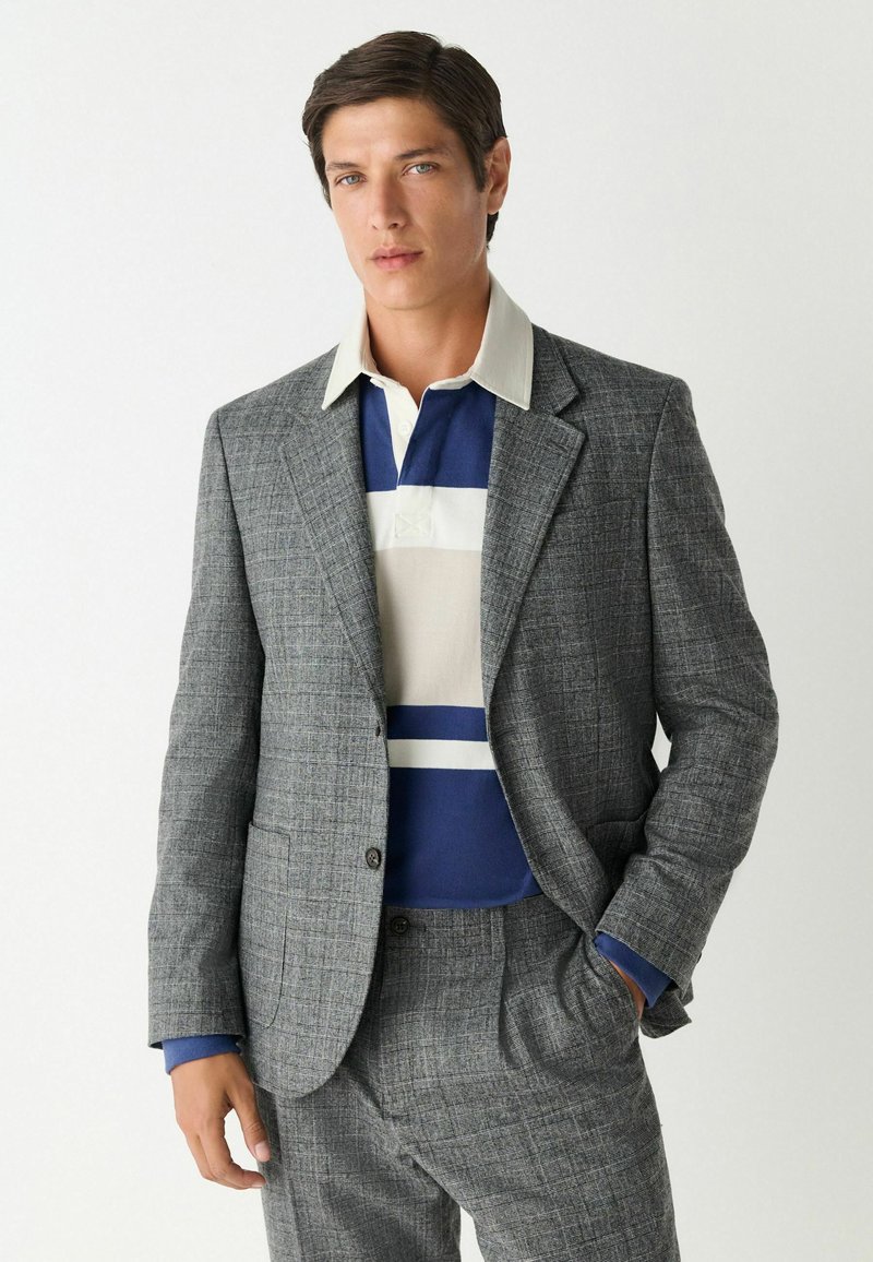 Grijze geruite blazer met notch lapels over een blauw-wit gestreept polo. Tailored fit met een gestructureerde stof en zijzakken.
