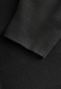 Tejido negro de punto con textura acanalada. Primer plano de secciones superpuestas que muestran patrones variados y bordes suaves.