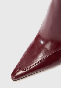 Bourgogne læder støvle med spids tå og blank overflade, der har slanke syninger og en glat finish langs den øverste sektion.