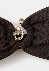 Chouchou en tissu brun foncé texturé avec une pince brillante en forme abstraite dorée reliant les deux extrémités froncées.