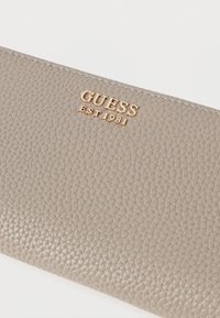 Halli nahast rahakott, millel on tekstuuriga pind. Esiküljel kuldse "GUESS EST 1981" logoga embossitud. Stiilne ja minimalistlik disain.