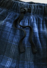 Blauwe geruite pyjamashorts van textuurstof met een elastische tailleband en zwarte trekkoorden. Heeft een ruitpatroon in verschillende blauwtinten.
