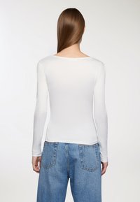 Biała bluzka z długim rękawem i okrągłym dekoltem, wykonana z gładkiego materiału. Połączona z niebieskimi dżinsami o wysokim stanie i klasycznym kroju.