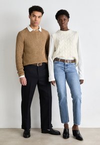 Strikket brun genser med hvit krage, kremfarget kabelstrikket vest, svarte vide bukser, lyseblå jeans, og svarte hælede mules.