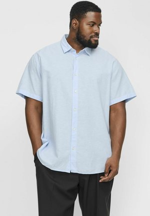 Himmelblaues kurzärmliges Button-Up-Hemd mit weicher Textur, mit Kragen, Frontknöpfen und lockerer Passform. Getragen mit schwarzen Hosen.