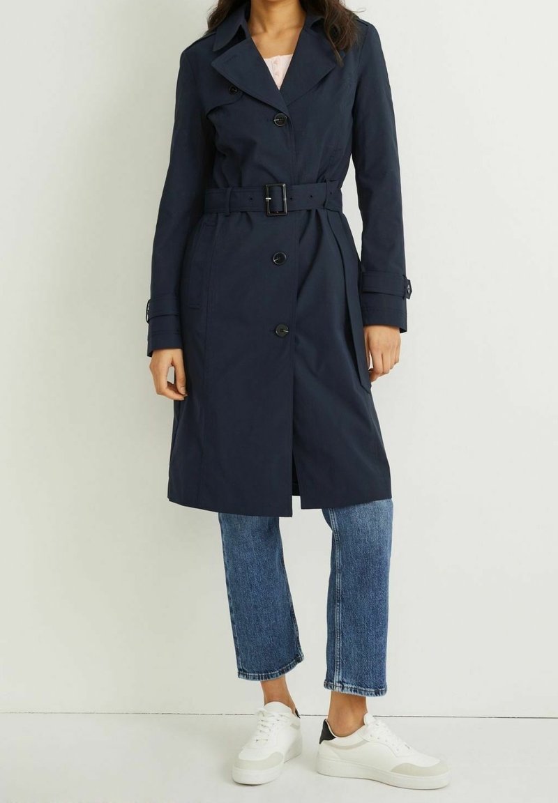 Granatowy płaszcz trencz z paskiem w talii, dużym kołnierzem i zapięciem na guziki. Noszony z jasnoniebieskimi, krótkimi dżinsami i białymi trampkami.
