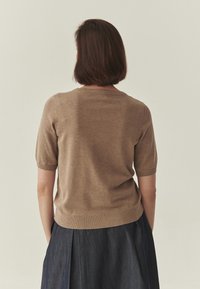 Pull marron à manches courtes en matière douce et texturée. Il présente un col rond et des poignets côtelés, assorti à une jupe en denim foncé.