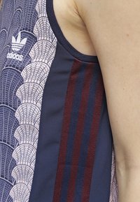 Sportovní tílko bez rukávů s námořnickým podkladem, růžovými vzorovanými akcenty a vínovými pruhy na stranách. Měkká textilie.