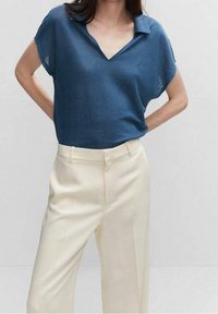 Modrý lehký pletený polo top s výstřihem do V a krátkými rukávy, v kombinaci s krémovými kalhotami na míru se rovný střihem a jemným záhybem.
