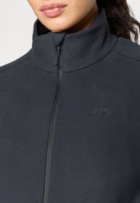 Svart fleecejacka med hög krage, hel dragkedja och broderad logotyp. Har mjuk textur och rena designlinjer.