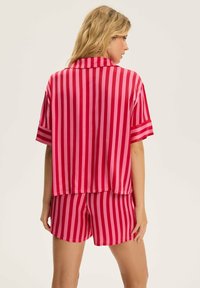 Koszulka z krótkim rękawem w różowo-czerwone paski oraz pasujące szorty z lekkiego materiału, charakteryzujące się luźnym krojem i gładką fakturą.