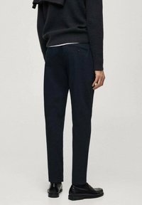 Pantaloni navy dintr-un material neted, cu o croială slim, buzunare la spate și detalii de cusătură subtile, asortați cu pantofi negri.