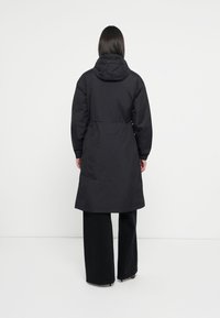 Black long parka jacket with a hood, cinched waist, and long sleeves. Made from a smooth, water-resistant material.