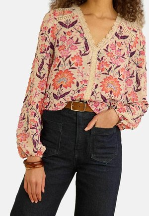 Mujer con blusa de estampado floral con encaje, metida dentro de unos vaqueros negros de cintura alta con bolsillos delanteros de parche y un cinturón marrón.