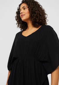 Black, flowy dress with a V-neck, short batwing sleeves, and gathered waist. The texture appears soft and lightweight, suitable for casual wear.
