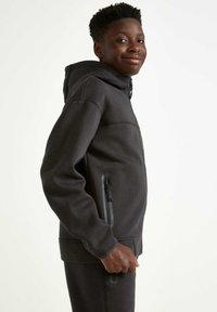 Dunkelgrauer Hoodie aus weichem Material, mit einem Frontreißverschluss, seitlichen Reißverschlusstaschen und einem lässigen Schnitt.