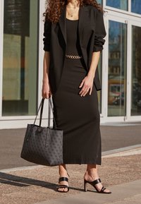 Sort ribbet kjole matchende med en oversized sort blazer, guld kædebælte, sort tote taske med logo mønster og sorte slidssandaler.