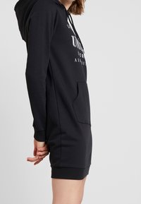 Robe à capuche noire en tissu doux, dotée d'une poche kangourou, d'une capuche réglable avec cordon de serrage et de poignets côtelés à l'ourlet.