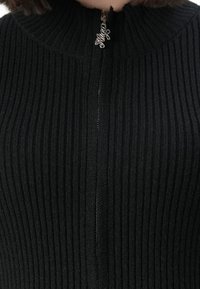 Black ribbed knit sweater with front zipper featuring a silver pull tab shaped as the word "Julian".