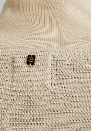 Beige gebreide trui met een gestructureerd patroon, een effen stuk en een klein zwart label met "PME Legend" in oranje.