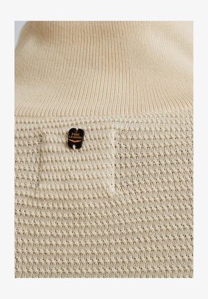 Beige neulepaita, jossa on tekstuuripinta, kiinteä kangaspatch ja pieni musta etiketti, jossa lukee "PME Legend" oranssilla.