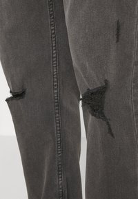 Sorte denim jeans med slitte detaljer og utfransede kanter ved knærne, samt kontrastsying langs sidesømmene.