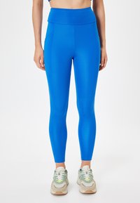 Blauwe hoge taille leggings van rekbaar materiaal. Voorzien van zijnaad voor een strakke pasvorm en gecombineerd met multikleurige sport sneakers.