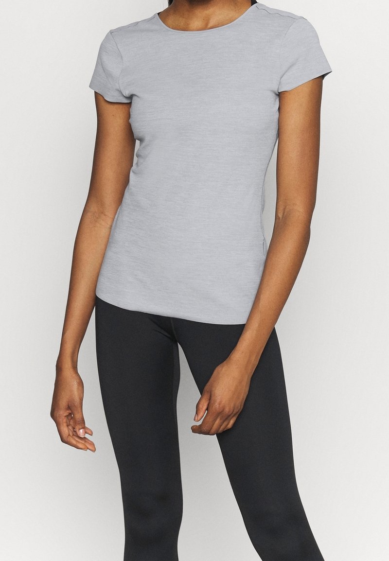 Grå kortärmad t-shirt med rund halsringning, tillverkad av ett slätt tyg, som matchas med svarta leggings. Passformen är skräddarsydd efter kroppen.