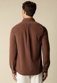 Bruine langarmshirt van zachte stof met knoopmanchetten en een schouderdetail op de rug. Glad oppervlak, klassiek kraagontwerp.