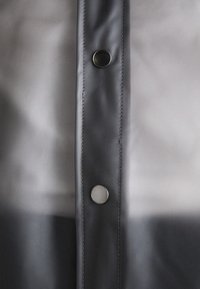 Vêtement d'extérieur gris avec une finition brillante, doté d'une fermeture à boutons et de coutures visibles sur le côté. Texture lisse avec un léger dégradé.